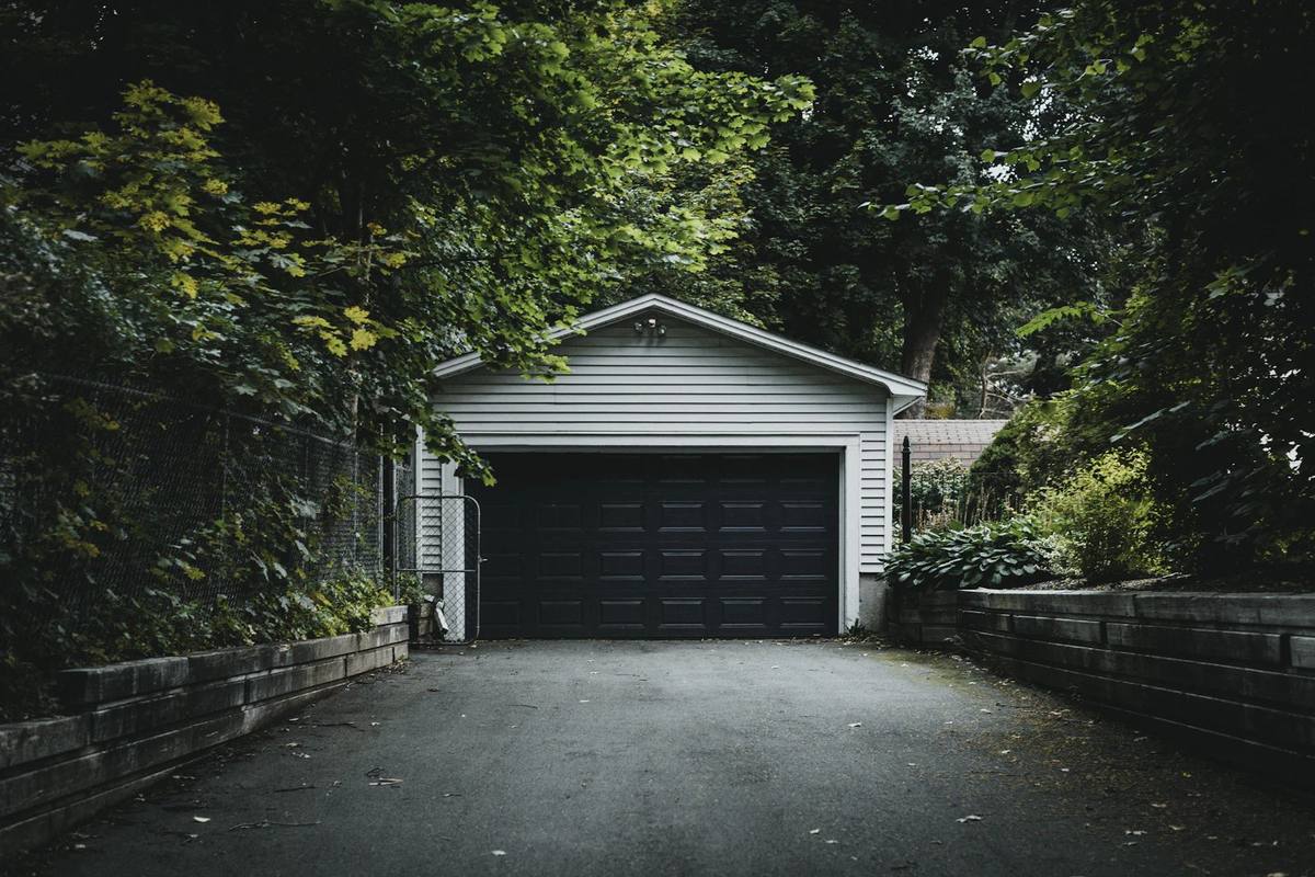Detached garage with a dark door at the end of a driveway